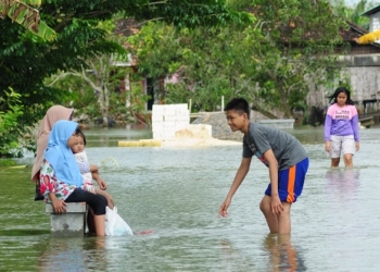 ILUSTRASI : Sejumlah warga tetap riang bermain paskahujan, meskipun desanya kebanjiran. (Nailin Risydan Al Anshori / Lingkarjateng.id)