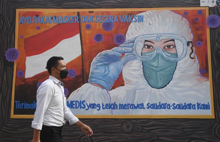 ILUSTRASI: Warga melintas di dekat mural bertema Covid-19. (Istimewa / Lingkarjateng.id)