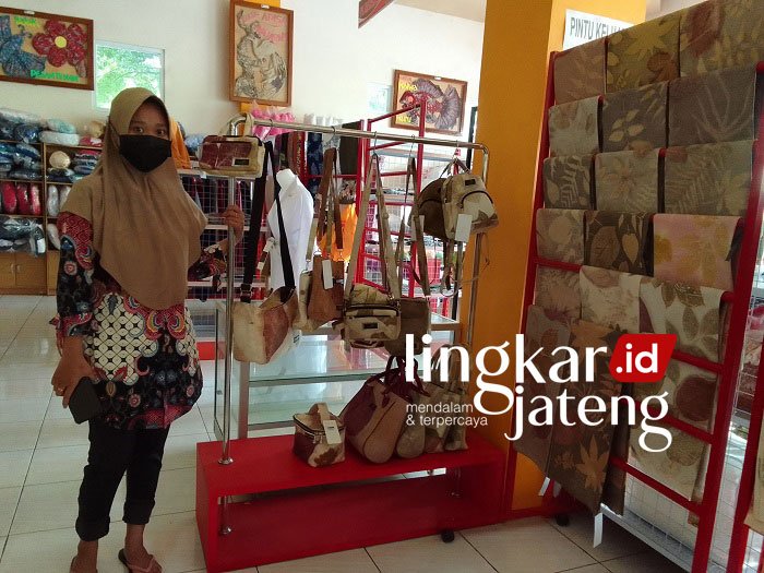 BERJUALAN: Salah satu pedagang kerajinan khas daerah di Pasar Pragolo Pati berfoto di samping dagangannya yang sepi pembeli. (Ayu Lestari/Lingkarjateng.id)