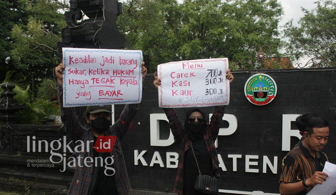 PROTES: Para peserta aksi memperlihatkan tulisan kritik menggelitik saat unjuk rasa seleksi perades di Kabupaten Blora. (Lilik Yuliantoro/Lingkarjateng.id)