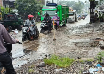 TERGENANG: Pengendara saat melintas jalan yang tergenang akibat perbaikan saluran air yang mangkrak.