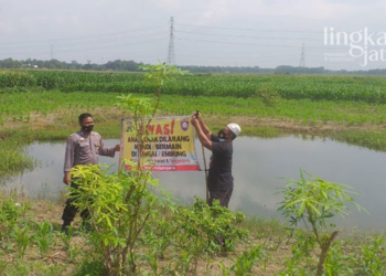 MEMASANG: Anggota Polsek Tanggungharjo Grobogan memasang spanduk larangan mandi dan bermain di embung, Minggu (13/3). (Muhamad Ansori/Lingkarjateng.id)