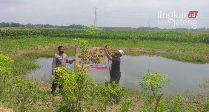 MEMASANG: Anggota Polsek Tanggungharjo Grobogan memasang spanduk larangan mandi dan bermain di embung, Minggu (13/3). (Muhamad Ansori/Lingkarjateng.id)