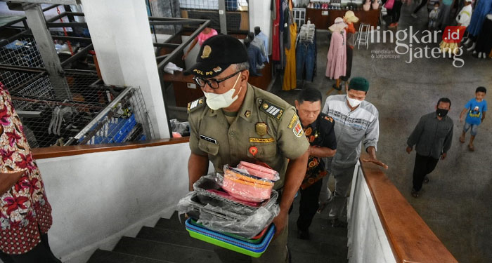 GOTONG ROYONG: Salah satu anggota Satpol PP Kota Semarang saat membantu pedagang memindahkan barang dagangan. (Dinda Rahmasari/Lingkarjateng.id)