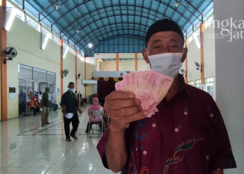 SENANG: Seorang warga sedang menunjukkan BLT minyak goreng dan BPNT yang diambil di Balai Desa Jurang, Kecamatan Gebog, Kudus. (Nisa Hafizhotus Syarifa/Lingkarjateng.id)