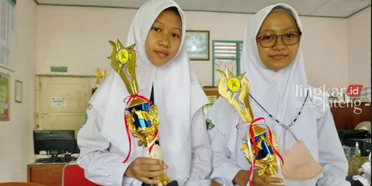 BERPRESTASI: Dua siswi MTs N 3 Pati, Amiroh Laluna Isabella (kiri) dan Andini Naila Hamida (kanan) memamerkan piala yang diraih pada ajang Kompetisi Sains Madrasah (KSM). (Arif Febriyanto/Lingkarjateng.id)