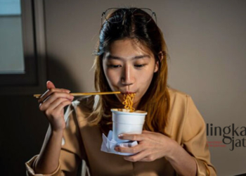 ILUSTRASI: Seorang wanita menyantap mi instan untuk makan malam sambil mengerjakan tugas. (Freepik @graphixchon/Lingkarjateng.id)