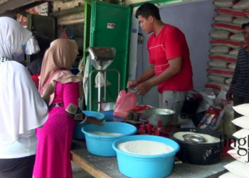 MENJUAL: Penjual beras di pasar tradisional Kendal sedang menimbang beras. (Arvian Maulana/Lingkarjateng.id)