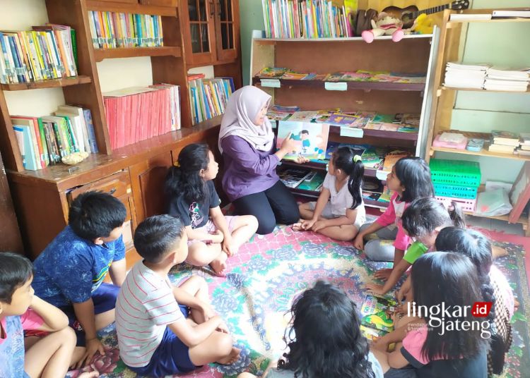 BELAJAR: Mahasiswi UNS Surakarta, Mega Herawati, mengajak anak-anak melatih kebiasaan membaca di taman baca Sijali Project, Singojayan, Tingkir Tengah, Tingkir, Salatiga. (Angga Rosa/Lingkarjateng.id)