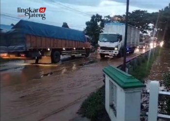 TERGENANG: Kendaraan berat melintas dengan hati-hati akibat banjir menggenangi jalan Pantura Pati-Juwana. (Arif Febriyanto/Lingkarjateng.id)
