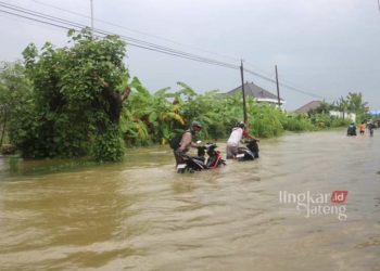 MOGOK: beberapa pengendara terpaksa mendorong kendaraan lantaran mogok akibat menerobos banjir di Pati. (Setyo Nugroho/Lingkarjateng.id)