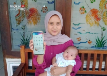 Ida Praistika (26), perempuan asal Desa Pulorejo, Kecamatan Winong, Kabupaten Pati, bersama buah hatinya menunjukkan Jaminan Kesehatan Nasional (JKN) Mobile miliknya pada Sabtu, 22 Juni 2024. (Setyo Nugroho/Lingkarjateng.id)