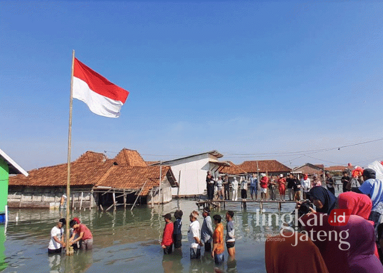 Warga Desa Timbulsloko, Kecamatan Sayung, Kabupaten Demak, Jawa Tengah, melaksanakan upacara peringatan Hari Ulang Tahun (HUT) ke-79 Republik Indonesia (RI) di tengah kepungan banjir rob pada Sabtu, 17 Agustus 2024. (M. Burhanuddin Aslam/Lingkarjateng.id)