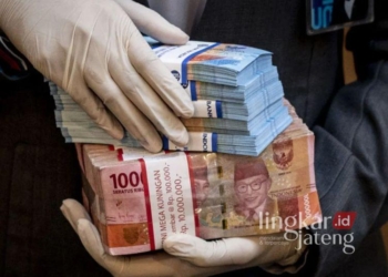 ILUSTRASI: Karyawan bank memegang uang pecahan Rp50.000 dan Rp100.000. (Antara/Lingkar.news)