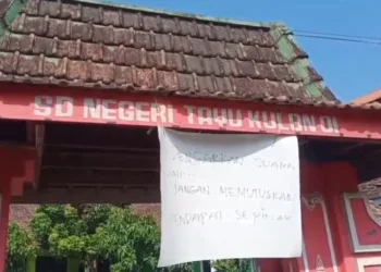 Tulisan penolakan kebijakan regrouping yang ditempelkan di Gapura SDN Tayu Kulon 1, Kabupaten Pati. (Mutia Parasti/Lingkarjateng.id)