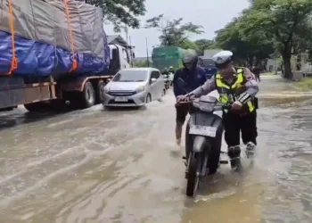 Petugas kepolisian membantu mendorong motor yang mogok lantaran menerjang banjir di Jalan Pantura Pati-Rembang di wilayah Kecamatan Batangan, Kabupaten Pati, Senin, 27 Oktober 2025. (Mutia Parasti/Lingkarjateng.id)