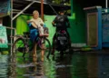 Seroang ibu menuntun sepedanya melintasi jalanan yang digenangi banjir di Kota Semarang. (Humas Pemprov Jateng/Lingkarjateng.id)