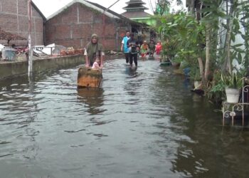 Warga Desa Sayung, Kecamatan Sayung, Kabupaten Demak, menerjang banjir yang masih merendam jalan desa setempat, Rabu, 28 Januari 2026. (M. Burhanuddin Aslam/Lingkarjateng.id)