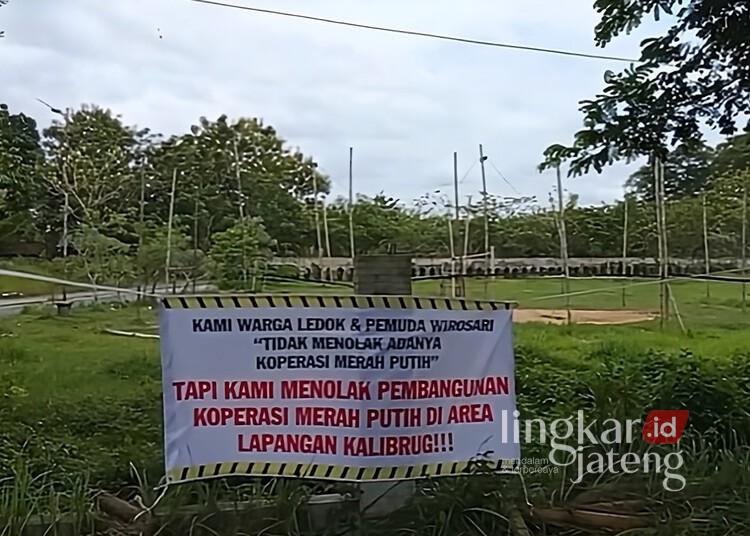 Warga Wirosari Grobogan Tolak Pembangunan Gerai Koperasi Merah Putih di Lapangan 25 Spanduk penolakan pembangunan Gerai Koperasi Merah Putih di Lapagan Kalibrug, Kelurahan Wirosari, Kecamatan Wirosari, Kabupaten Grobogan, Selasa, 27 Januari 2026. (Ahmad Abror/Lingkarjateng.id)