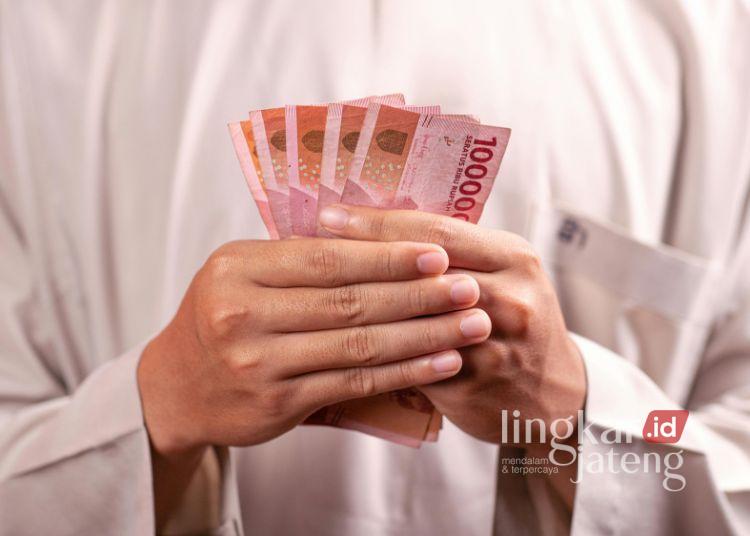 Perusahaan di Salatiga Terlambat Bayar THR 2026 Terancam Denda 5 Persen 25 ILUSTRASI: Seseorang memegang uang pecahan Rp100.000. (Canva)